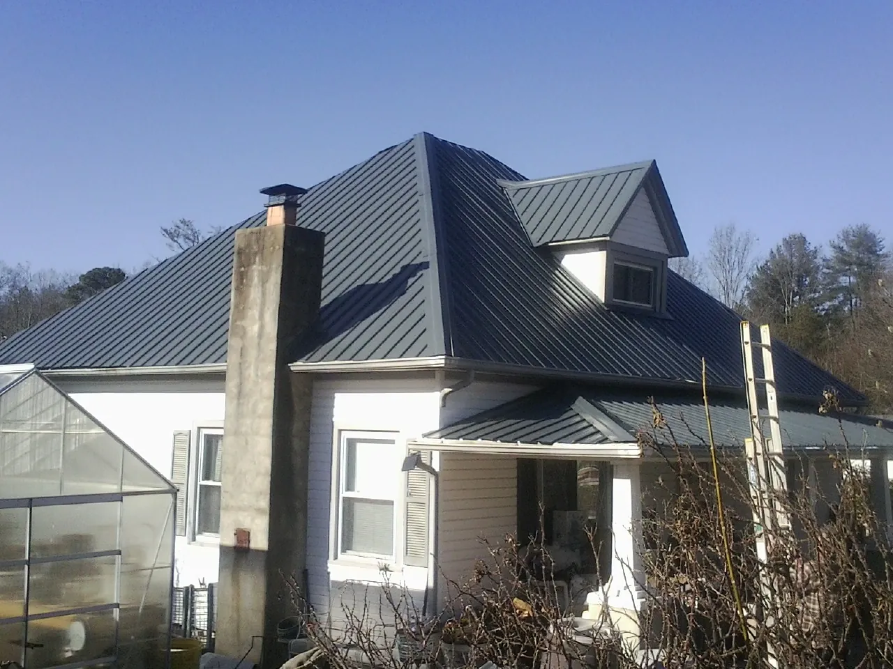 Dark blue standing seam metal roof on a white farmhouse with dormer — Slate & Tile Roof Repair by Roofing Brothers in Norton