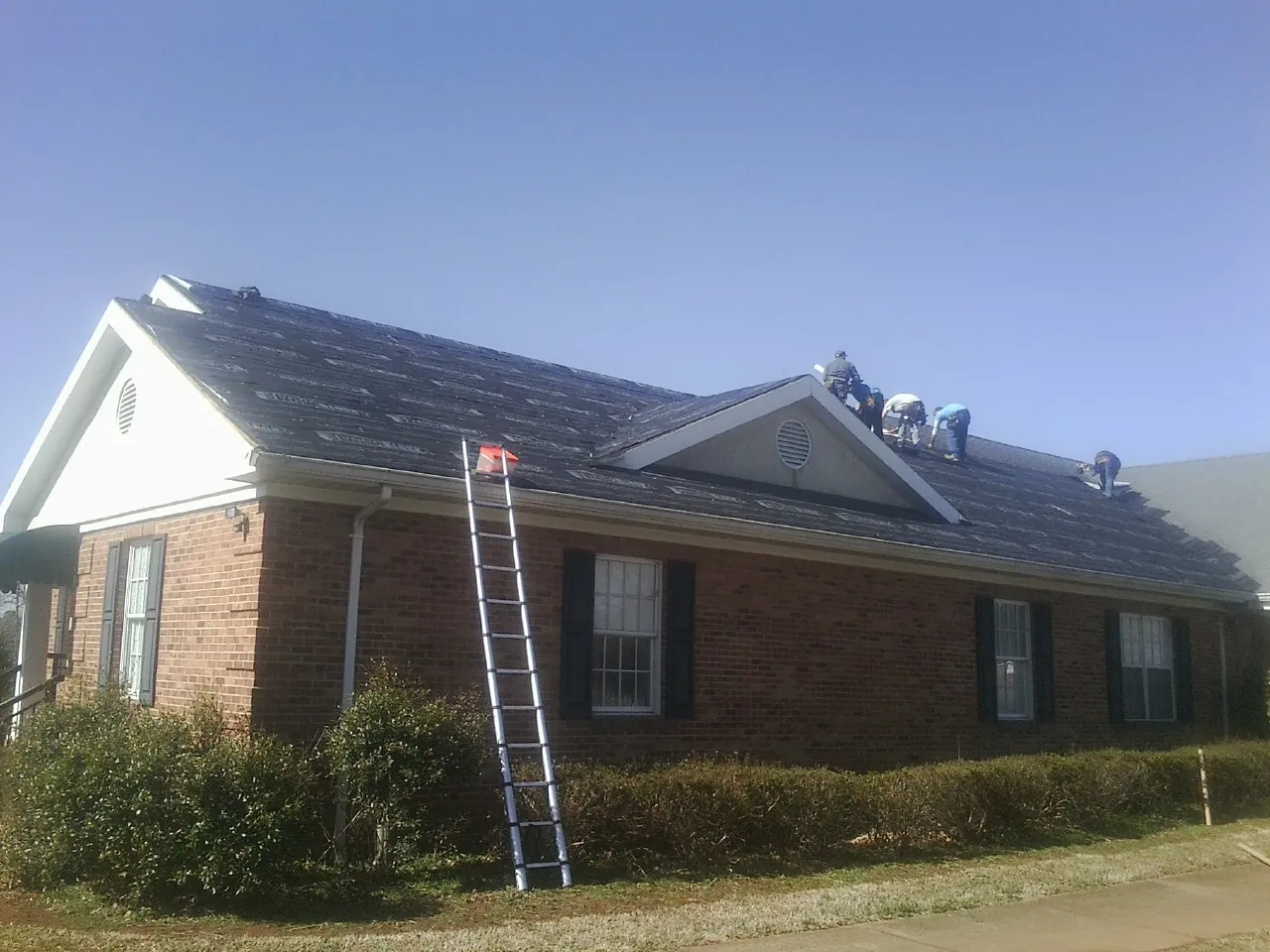 Crew tearing shingles off a brick ranch roof with a ladder set — Emergency Roof Repair work by our crew in Norton